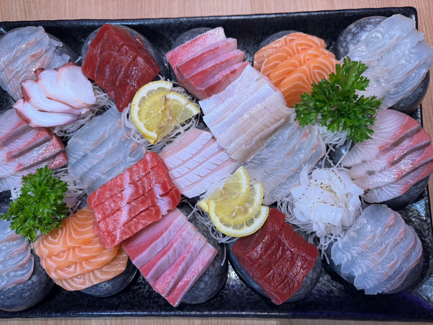 Top-down phone photo of a full sashimi spread: red tuna, orange salmon and white fluke on black stone plates